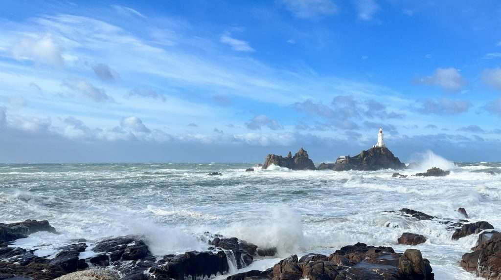 Corbiere Lighthouse Jersey - Assurify Consulting A photo of Corbiere Lighthouse taken from the shore at high tide on a sunny windy day