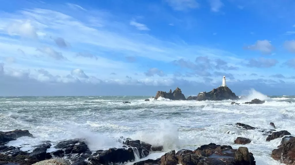 A photo of Corbiere Lighthouse taken from the shore at high tide on a sunny windy day